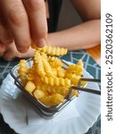 Hand taking tasty, crispy and golden crinkle cut potato french fries from the basket. Eating fried fast food snack, side dish or appetizer. Unhealthy eating concept