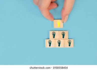 Hand taking a wooden cube with the yellow light bulb symbol on pastel blue background. New business idea, innovation and solution concept. - Shutterstock ID 1930558454