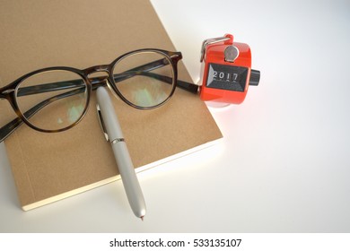 Hand tally counter with notebook, pen and glasses on white background.  2017 New year concept