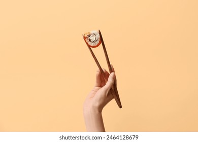 Hand with tasty sushi roll and chopsticks on beige background - Powered by Shutterstock