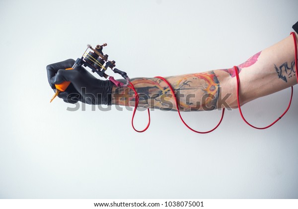 hand tattoo artist with the tattoo machine on a\
white background. the red\
wires
