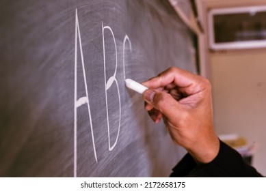 A hand of a teacher writing the ABC alphabet on the blackboard with chalk in an English lesson.  - Shutterstock ID 2172658175