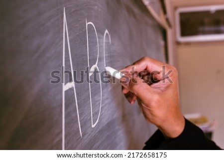 A hand of a teacher writing the ABC alphabet on the blackboard with chalk in an English lesson. 