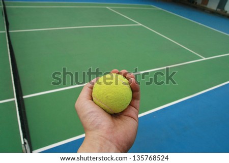 hand and tennis ball ,tennis ball on green blue court and net in sport competition background, sport club