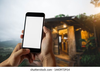 Hand That Are Holding A Black Phone With A Blank White Screen In The Morning Light Of An Air Residence.