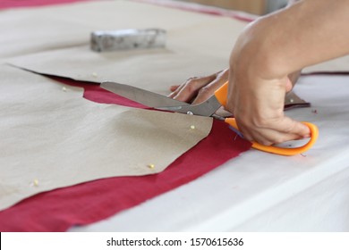 The hand that is using the scissors to cut the cloth