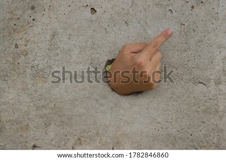 The hand that went through the concrete wall points to the corner of the wall with a finger.