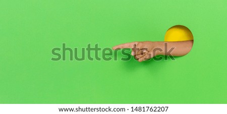 Hand through hole in light green background pointing with finger to something, showing direction sign