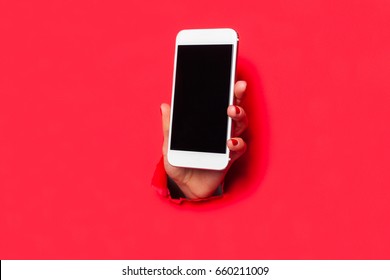 Hand Through Hole In Red Cardboard Sheet Showing The Screen On Smartphone. 