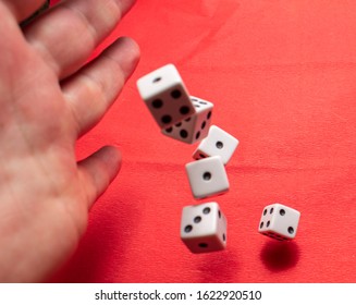 Hand Throwing Dice, Hoping For The Best Odds. Six Dice On Red Background