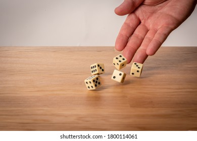 Hand throwing five dice on a wooden table - Shutterstock ID 1800114061