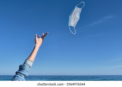 Hand throwing a mask in the air as a sign of freedom after receiving the vaccine, end of the pandemic, mask-free holidays, end of covid-19, normal life post-pandemic, virus-free summer - Shutterstock ID 1964976544