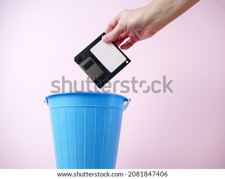Hand throwing old floppy disk away, trash bin electronic gadget inside, phone in trashcan, concept