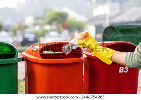  Hand throwing plastic bottle into trash bin, waste disposal concept.