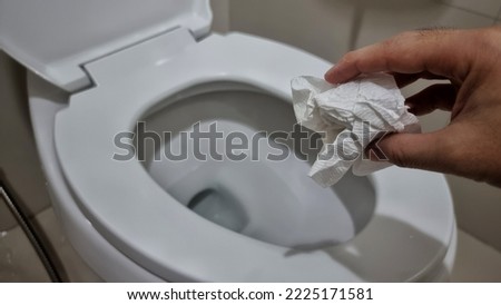 Hand throwing tissue paper directly in the toilet bowl.
