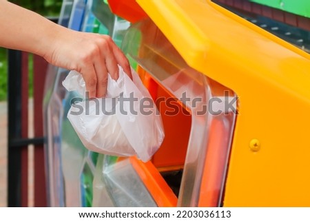 Hand throws away garbage into trash container. The yellow bin for general waste material.