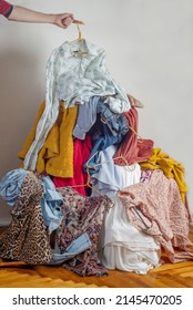 Hand wirft Kleidung in einen Haufen mit gebrauchten Kleidern. Das Konzept der nachhaltigen Mode. Pile von gebrauchten Kleidungsstücken auf hellem Hintergrund. Wiederverwertung