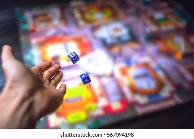 Hand throws the dice on the background of colorful blurred fantasy Board games, gaming moments in dynamics