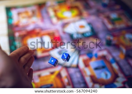 Hand throws the dice on the background of colorful blurred fantasy Board games, gaming moments in dynamics