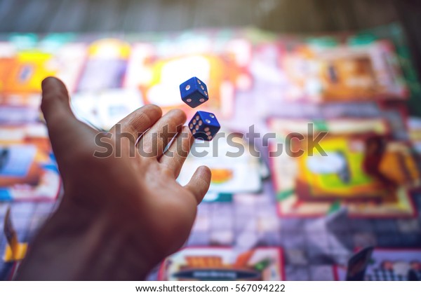Hand throws the dice on\
the background of colorful blurred fantasy Board games, gaming\
moments in dynamics