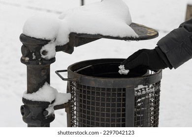 Hand Throws Out Garbage in Winter Park, Throwing Paper Garbage into Snowy Street Trash Can Closeup, Clean City Concept, Blurred Background