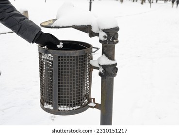 Hand Throws Out Garbage in Winter Park, Throwing Paper Garbage into Snowy Street Trash Can Closeup, Clean City Concept, Blurred Background