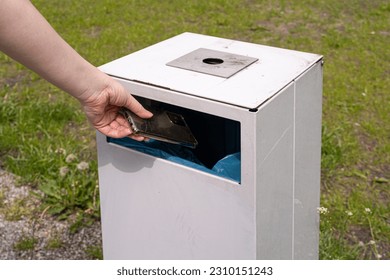 Hand Throws out Smartphone, Throwing Electronic Device into Street Trash Can, Throwed Away Smartphone, Dangerous Garbage Concept, Blurred Background