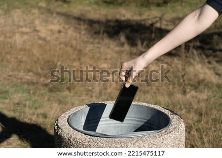 Hand throws out smartphone. Throwing electronic device into street trash can, throwed away smartphone, dangerous garbage concept, blurred background