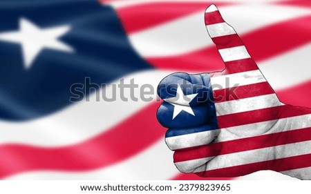 hand with thumbs up in approval with the Liberian flag painted. Image with flag background area out of focus, copy space area
