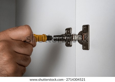 Hand tightening cabinet hinge using screwdriver. Furniture assembly, home repair and maintenance concept.
