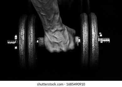 A Hand Tightly Gripping A 22kg Dumbbell Revealing Bulbous Veins In The Back Of The Hand And Wrist. Black And White. No Obvious Branding.