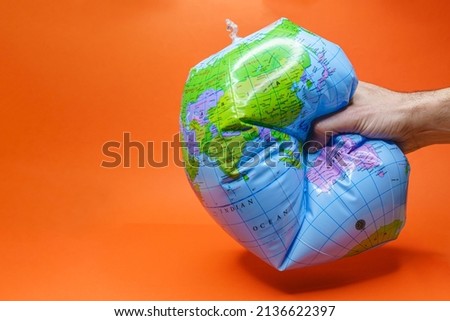 Hand tightly gripping an earth globe on orange background.