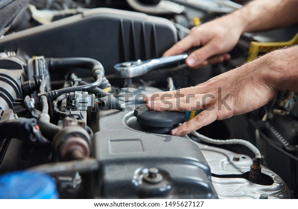Hand with tool on car engine during inspection\
or maintenance in a\
workshop