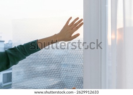 Hand touching bubble wrap on window during sunset, capturing a moment of peace and creativity