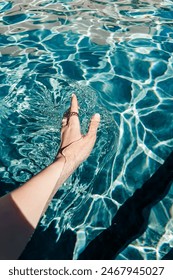 Hand touching pool surface with sun ripple on the water, summer lifestyle