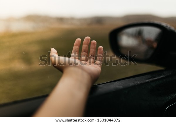 Hand touching rain drops. Mirror seen through the\
glass. Wet car window. Close up rain drop. Car view see the mirror.\
Rainy day.