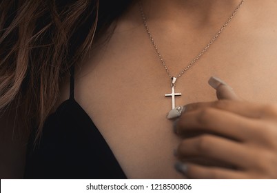 A hand touching a valuable Christ Cross made of silver on a beautiful piece of jewelry.