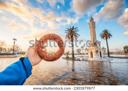 Hand with traditional simit turkish round bagel bread with clocktower on Konak Square in Izmir city during majestic sunset