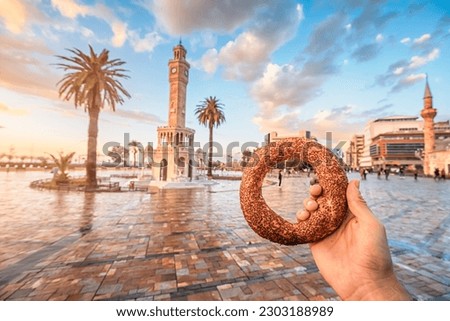 Hand with traditional simit turkish round bagel bread with clocktower on Konak Square in Izmir city during majestic sunset