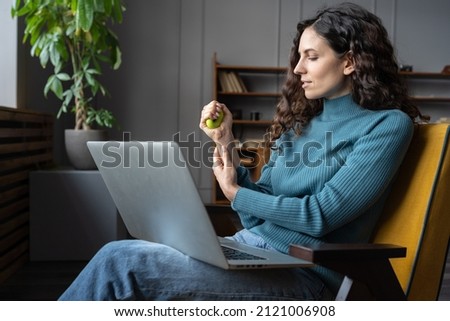 Hand training at work. Focused concentrated young woman using fitness equipment at workplace, female office worker exercising with silicone grip ring to strengthen fingers, hands, wrists and forearms