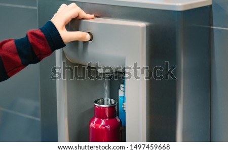 Hand of a traveler pressed the button of drinking water filling station at the Airport, Refill, Reusable bottle.  Eco friendly, Environmental awareness, Clean water, Zero waste, Plastic free july.