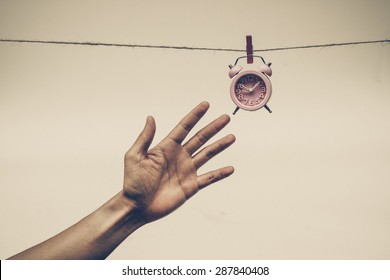 Hand Trying To Catch A Clock Hung On A Rope - Time Waits For No Man Concept