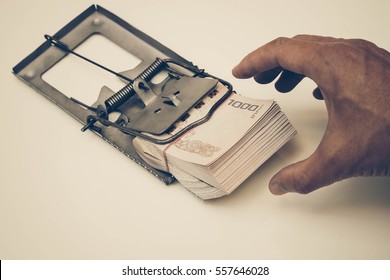 Hand Trying To Pick Up A Pile Of Thai Baht Banknotes From A Mouse Trap / Money Trap / Debt