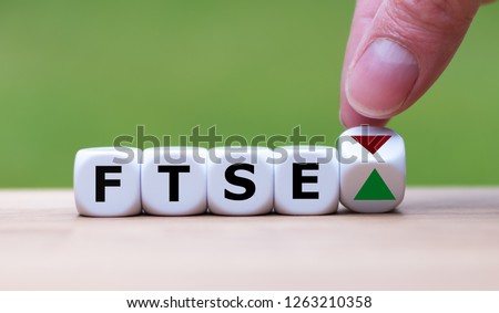 Hand is turning a dice and changes the direction of an arrow symbolizing that the FTSE 100 Index is changing the trend and goes up instead of down (or vice versa)