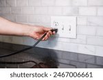 Hand Turning Off Light Switch with Electrical Outlet in Background