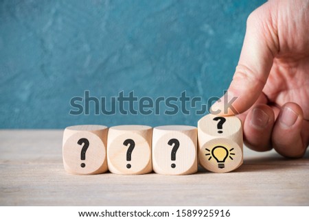 hand is turning one of many cubes with questionmarks to find an idea symbol on wooden background