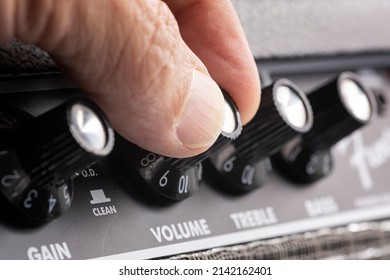 hand turning up the volume of a guitar amplifier, treble and bass control knobs out of focus , equalization dials close up, horizontal