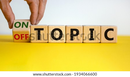 Hand turns a cube and changes the expression 'off topic' to 'on topic'. Beautiful yellow table, white background. Business concept. Copy space.
