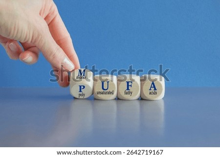 Hand turns cube and form the acronym MUFA (Monounsaturated Fatty Acids) and PUFA (Polyunsaturated Fatty Acids). Beautiful blue background, grey table. Business and medical concept. Copy space.