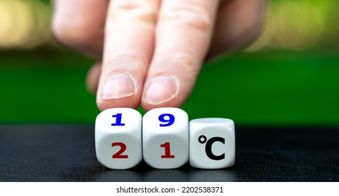 Hand turns dice and changes the expression "21 degrees Celsius" to "19 degrees Celsius". Symbol for lowering the temperature in offices to reduce the energy consumption. - Shutterstock ID 2202538371